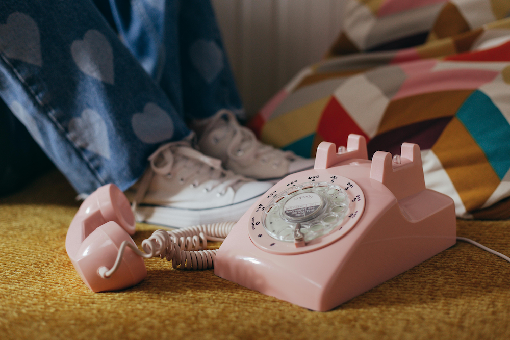 A photo of a pink rotary telephone on a carpeted floor