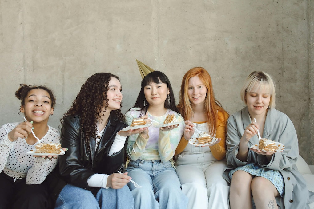 A group of young teenage woman are sitting next to each other celebrating a birthday.