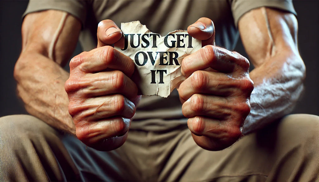 A close-up of human hands firmly holding a torn piece of paper with the words "Just Get Over It" written on it, symbolizing defiance against dismissive phrases.