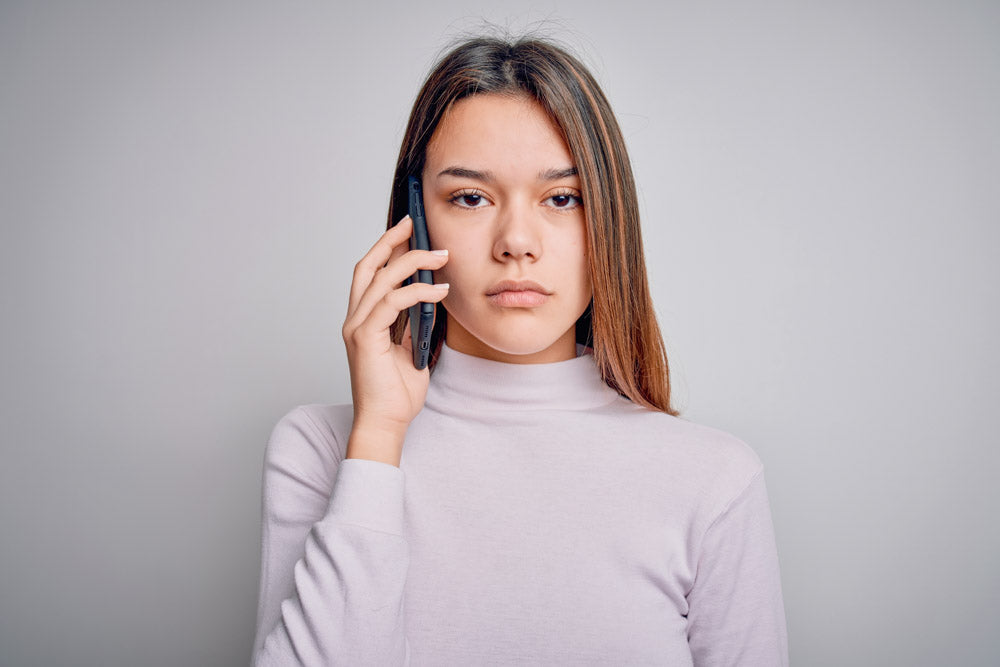 Things not to say to someone with anxiety: a photo of a young woman looking intently at the camera holding a mobile phone to her right ear.