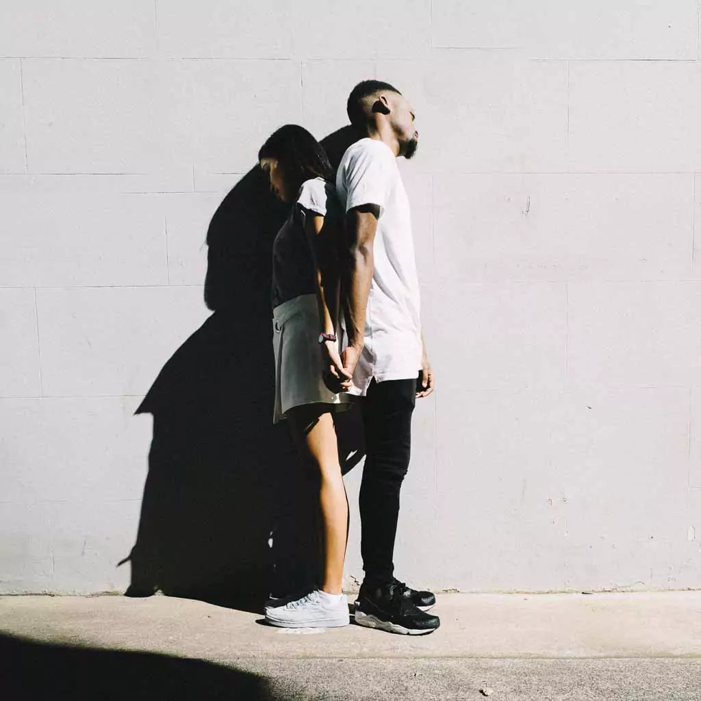 Image forTwo people standing back-to-back against a brick wall, symbolizing support and solidarity during difficult times. an article: 