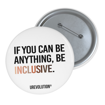 A photo of a 3" white Be Inclusive Racial Diversity pin button promoting an end to racism. On the front of the pin button is the phrase: "If you can be anything, be inclusive," in black upper case letters. The text is all black, except the word "Inclusive," which is in different skin colors, with the lightest color on the left and the darkest on the right. 