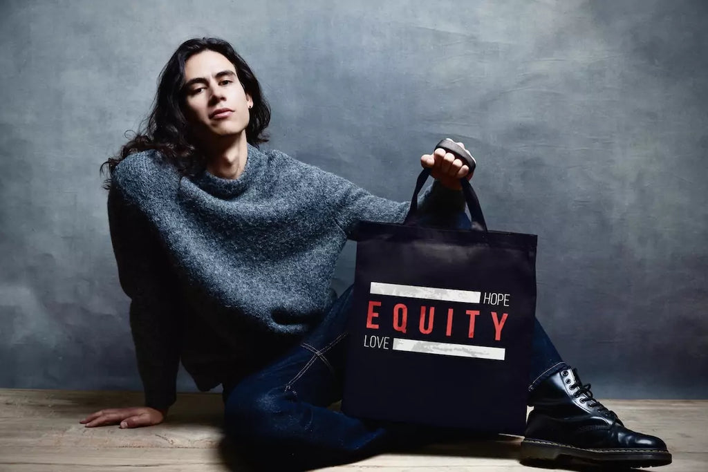 Model holding a black tote bag with bold red ‘EQUITY’ design, representing diversity, inclusion, and social justice. Shop diversity bags, totes, and backpacks.