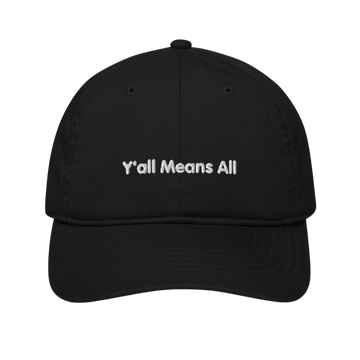 This is a photo of a black organic Y'all Means All cap lying flat against a plain background. On the front panel of the cap the phrase, 'Y'all Means All,' is embroidered on it in white upper case letters.