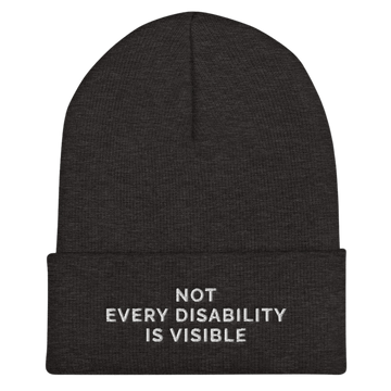 A photo of a dark gray hypoallergenic Not Every Disability Is Visible Beanie lying flat against a plain background. On the cuff of the beanie the phrase, 'Not Every Disability Is Visible,' is embroidered on it over three lines in white upper case letters.